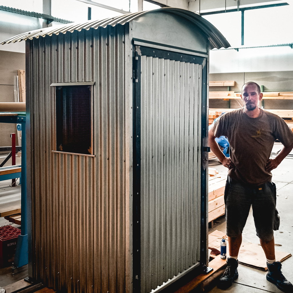 Freier Texter Stefan Jonies in Handwerker-Kleidung steht bei Haus aus Wellblech